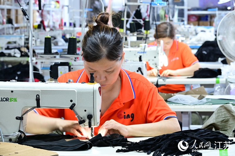 当地一家企业车间内，女工正在赶制服装。人民网 张瀚天摄
